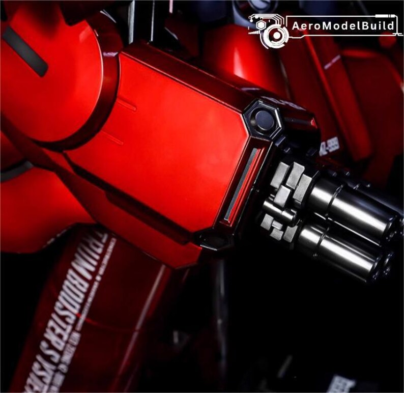 May include: Close-up of a red and black model kit component. The image features a metallic red arm with a silver gun barrel and the text "TRIM BOOSTER SYSTEM". The AeroModelBuild logo is visible in the top right corner.