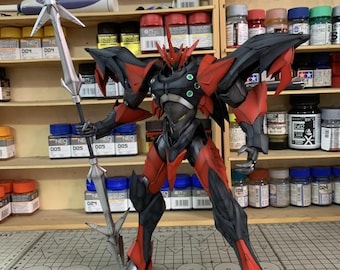 May include: A detailed model of a red and black robot warrior, holding a silver spear and sword. The robot has intricate armor and is posed in a dynamic stance. The background includes shelves with paint bottles and model supplies.