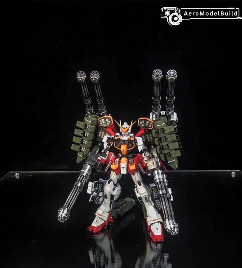 K&ouml;nnte beinhalten: Ein hochdetaillierter Gundam-Modellbausatz in Wei&szlig;, Rot und Orange mit umfangreicher Bewaffnung, darunter zwei gro&szlig;e, schultermontierte Kanonen und zwei handgef&uuml;hrte Gatling-Gesch&uuml;tze. Der Text AeroModelBuild ist oben zu sehen.