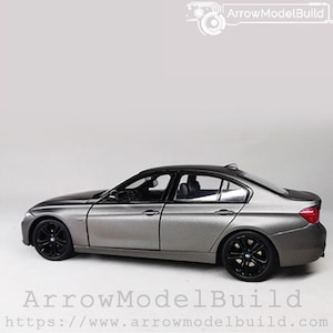 May include: A gray model car with black wheels and a black roof. The car has a sleek design and is set against a white background. The text "ArrowModelBuild" is visible in the image.