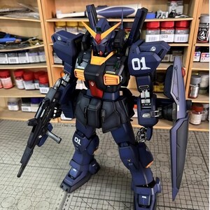 Pu&ograve; includere: Modello dettagliato di un robot mecha, principalmente blu navy con dettagli arancioni e rossi. Il robot &egrave; armato con un fucile e uno scudo e presenta il numero "01" sulla spalla e sulla gamba. Il modello &egrave; posizionato su una superficie a griglia.