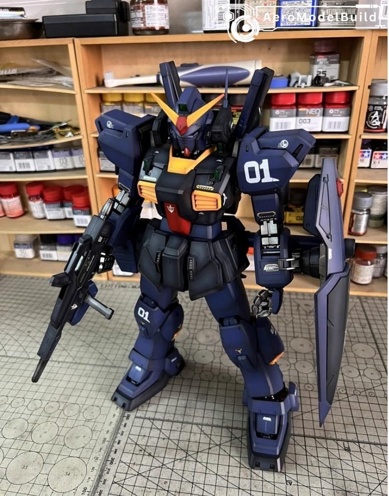Pu&ograve; includere: Modello dettagliato di un robot mecha, principalmente blu navy con dettagli arancioni e rossi. Il robot &egrave; armato con un fucile e uno scudo e presenta il numero "01" sulla spalla e sulla gamba. Il modello &egrave; posizionato su una superficie a griglia.