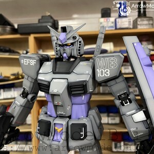 May include: A detailed model of a gray and purple mecha robot with the text "WB 103" and "EFSF" printed on the armor. The robot has a shield and is set against a blurred background of shelves.