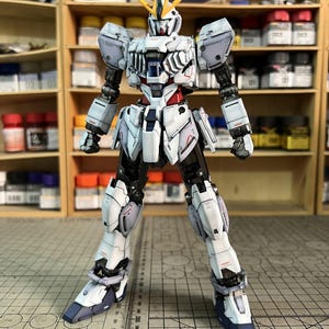 May include: A detailed model of a white, black, and blue robot with yellow accents. The robot is standing with its legs apart and arms at its sides. The model is on a cutting mat with measurements in inches. The text "ArrowModelBuild" is visible.