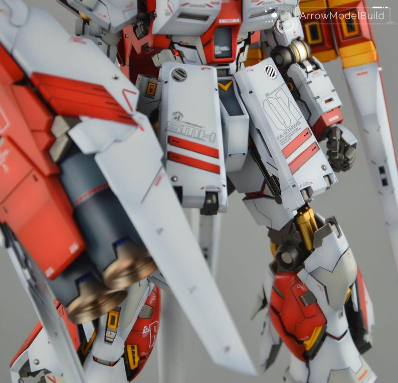 May include: Detailed model robot with white, red, and grey panels. The model features intricate mechanical details, including visible joints, vents, and text. The design incorporates red stripes and accents, with gold-coloured mechanical components.