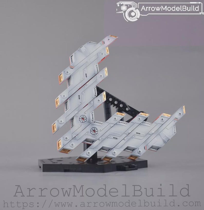 May include: A model kit of a futuristic spacecraft in white and grey, with gold and red accents. The model is mounted on a black base. The text "ArrowModelBuild" is visible.