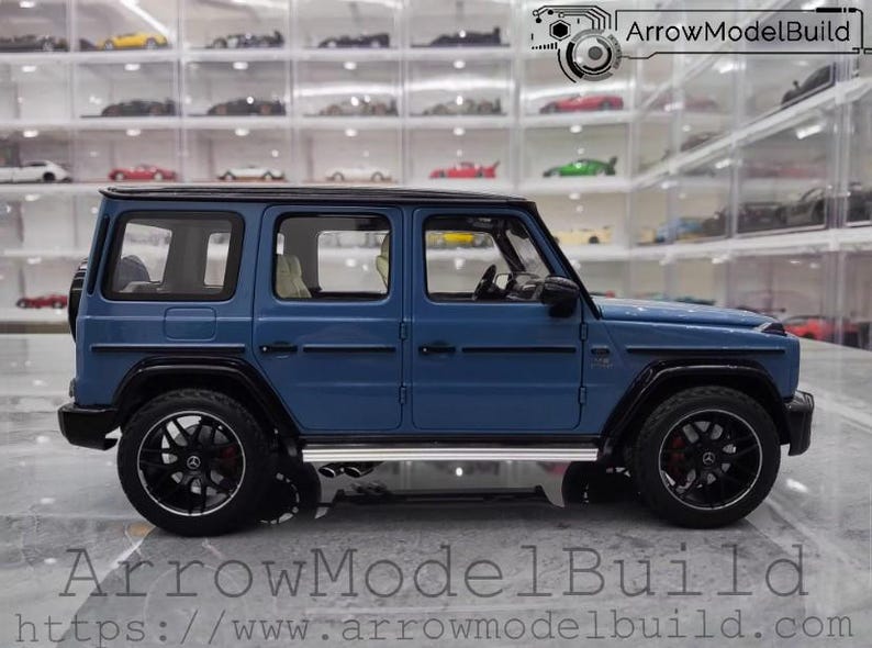 May include: A blue model SUV with black wheels and trim. The model car has a spare tire on the back and a silver running board. The text "ArrowModelBuild" and a website address are visible at the bottom of the image.