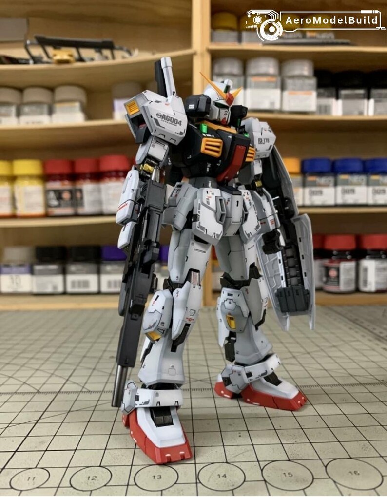 Pode incluir: Modelo detalhado de um rob&ocirc; Gundam, principalmente branco, cinza e preto, com detalhes em vermelho e amarelo. O modelo tem uma arma grande e um escudo. O texto "AG004" &eacute; vis&iacute;vel no ombro.