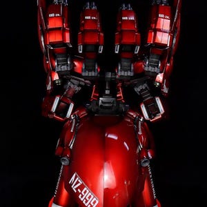 May include: A glossy red model of a robot with multiple articulated components. The model features the text "NZ-999" and "STER'S YSTEMLIZ" in white. The robot has a sleek, metallic finish and is set against a black background.