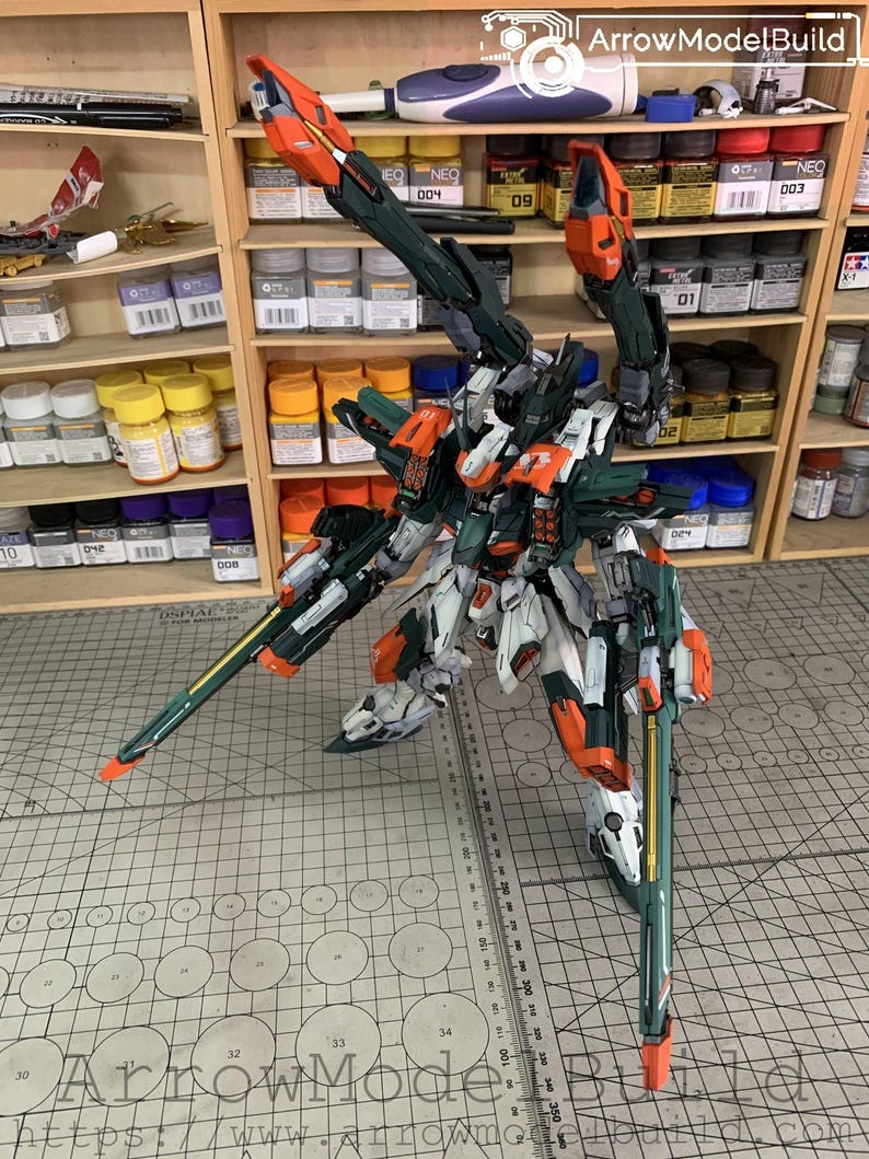 May include: A detailed model kit of a mech robot, featuring a color scheme of white, orange, and dark green. The model has intricate details and is posed on a cutting mat. Shelves filled with paint bottles are in the background.