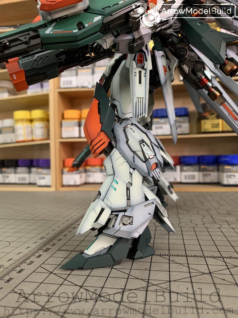 May include: A detailed model of a robot with a complex design. The robot features a color scheme of white, green, orange, and gray. The image includes the text "ArrowModelBuild" and a website address.