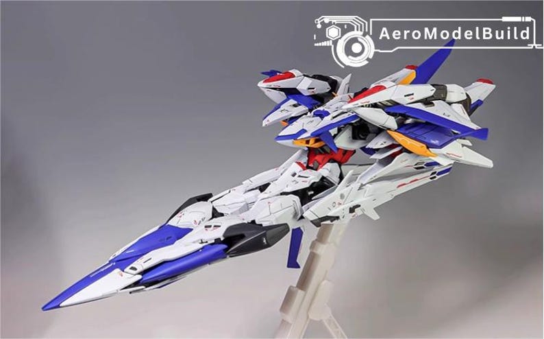 Puede incluir: Maqueta de avi&oacute;n AeroModelBuild. El modelo es blanco, azul, rojo y amarillo. El avi&oacute;n est&aacute; sobre un soporte transparente. El texto "AeroModelBuild" est&aacute; en la esquina superior derecha.