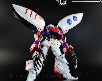 May include: A detailed model robot in white, red, blue, and purple, featuring large wing-like structures. The robot has intricate mechanical details, including articulated arms and legs. The image includes the text "ArrowModelBuild" and a website address.