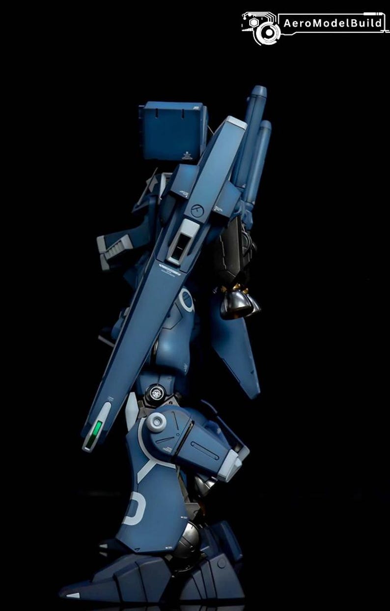 May include: A side view of a detailed, dark blue model robot with articulated joints and panels. The model has a complex design with various mechanical components, including a large weapon and a backpack. The text "AeroModelBuild" is visible in the upper right corner.