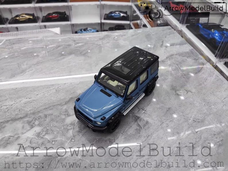 May include: A blue and black diecast model SUV. The model has a black roof, black tires, and silver side steps. The vehicle is on a marble-like surface. The text "ArrowModelBuild" and a website address are visible.