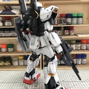 Op de afbeelding: Gedetailleerd model van een witte, zwarte en rode mecha-robot, met een geweer. De robot heeft een schild op zijn rug en staat op een oppervlak. Het model is zeer gedetailleerd met zichtbare paneellijnen en mechanische componenten.