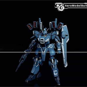 May include: A blue and white model robot with a shield and gun, set against a black background. The robot has multiple missile launchers and the text "AeroModelBuild" in the upper right corner.