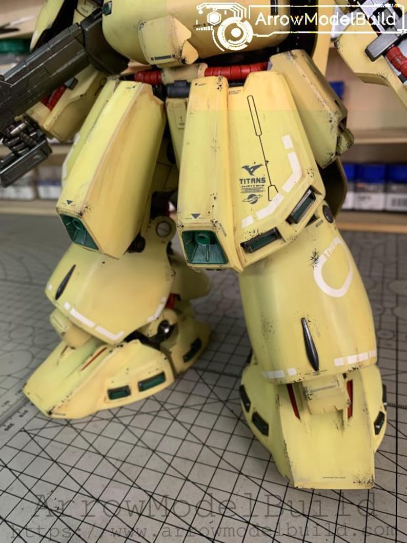 May include: Close-up of a yellow and white model robot's legs and lower torso. The model has a weathered appearance with black and brown accents. The word "TITANS" is visible on the leg.