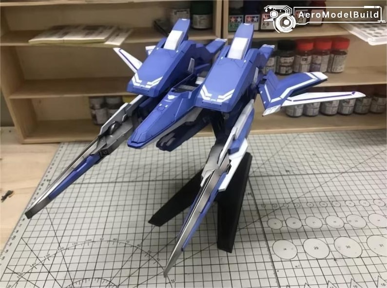 May include: AeroModelBuild model kit of a futuristic aircraft. The model is primarily blue and white, with silver accents. It features a dual-fuselage design and long, pointed wings. The model is displayed on a black stand.