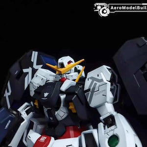 May include: A detailed close-up of a white, black, and red robot model. The model features intricate paneling, yellow accents, and a stylized head with a prominent crest. The text "AeroModelBuild" is visible in the top right corner.