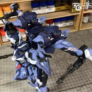 May include: A detailed, partially assembled model kit of a futuristic robot, primarily in shades of blue, white, and black. The model features intricate mechanical details, including articulated limbs and weapon attachments. The background shows shelves with paint bottles.
