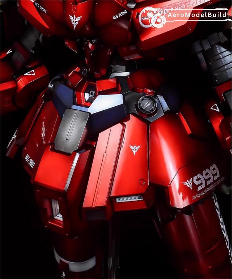 May include: A close-up of a red and black model robot with metallic details. The model has white logos and the text "NZ-999" and "999" printed on it. The text "AeroModelBuild" is also visible.