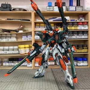 May include: A detailed model kit of a mech robot, predominantly white, green, and orange. The model has multiple articulated parts and is posed on a grid surface. The text "ArrowModelBuild" is visible.