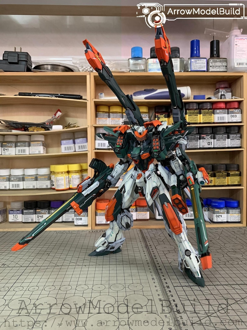 May include: A detailed model kit of a mech robot, predominantly white, green, and orange. The model has multiple articulated parts and is posed on a grid surface. The text "ArrowModelBuild" is visible.