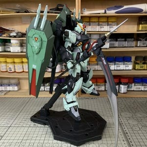 Puede incluir: Modelo detallado de un robot verde y negro, sosteniendo una gran espada y un escudo. El robot est&aacute; montado sobre un soporte negro. El escudo es verde con detalles rojos y blancos. El modelo est&aacute; en un taller.