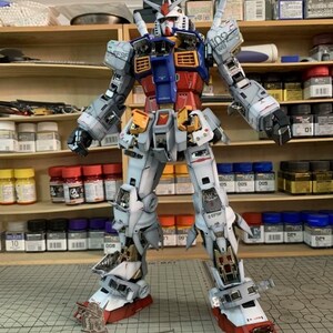 K&ouml;nnte beinhalten: Ein detailliertes Modell des RX-78-2 Gundam, ein Mecha-Roboter, wird gezeigt. Das Modell hat ein Farbschema aus Wei&szlig;, Blau, Rot und Gelb. Das Modell steht auf einer karierten Oberfl&auml;che, mit Farbt&ouml;pfen und Regalen im Hintergrund. Der Text "RX-78-2 GUNDAM" ist sichtbar.