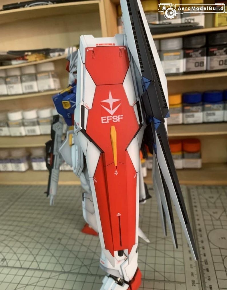 K&ouml;nnte beinhalten: Detailliertes Modell eines Mecha-Roboters, haupts&auml;chlich wei&szlig;, rot und blau. Der Roboter hat einen gro&szlig;en Schild mit dem Text "EFSF" und einem Sternemblem. Das Modell steht auf einer Rasteroberfl&auml;che, im Hintergrund Regale mit Farbe und Zubeh&ouml;r.