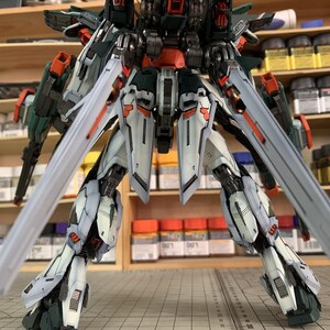 May include: A detailed model of a mech robot, featuring a complex design with multiple articulated parts. The robot is primarily white, with accents of dark green, orange, and black. The model has large, stylized blades extending from its back and legs. The text "ArrowModelBuild" is visible.