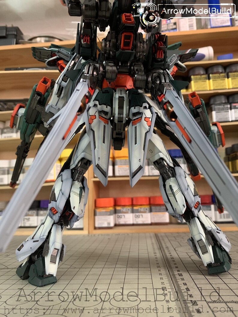 May include: A detailed model of a mech robot, featuring a complex design with multiple articulated parts. The robot is primarily white, with accents of dark green, orange, and black. The model has large, stylized blades extending from its back and legs. The text "ArrowModelBuild" is visible.