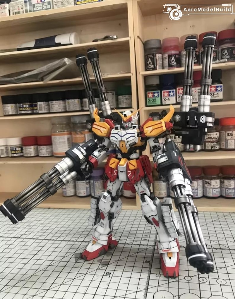 K&ouml;nnte beinhalten: Detailliertes Modell eines Gundam-Roboters mit wei&szlig;em, rotem, gelbem und schwarzem Farbschema. Der Roboter ist mit mehreren gro&szlig;en Kanonen ausgestattet und befindet sich in einer dynamischen Pose. Der Hintergrund zeigt Regale mit Farbt&ouml;pfen und Modellbauzubeh&ouml;r.
