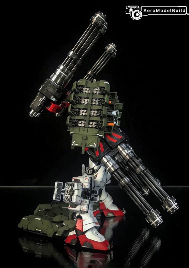 K&ouml;nnte beinhalten: Eine wei&szlig;e, rote und schwarze Roboter-Actionfigur mit zwei gro&szlig;en mehrl&auml;ufigen Gatling-Kanonen, einem gr&uuml;nen Raketenwerfer-Rucksack und an den Beinen montierten Waffensystemen. Der Text AeroModelBuild ist oben rechts zu sehen.