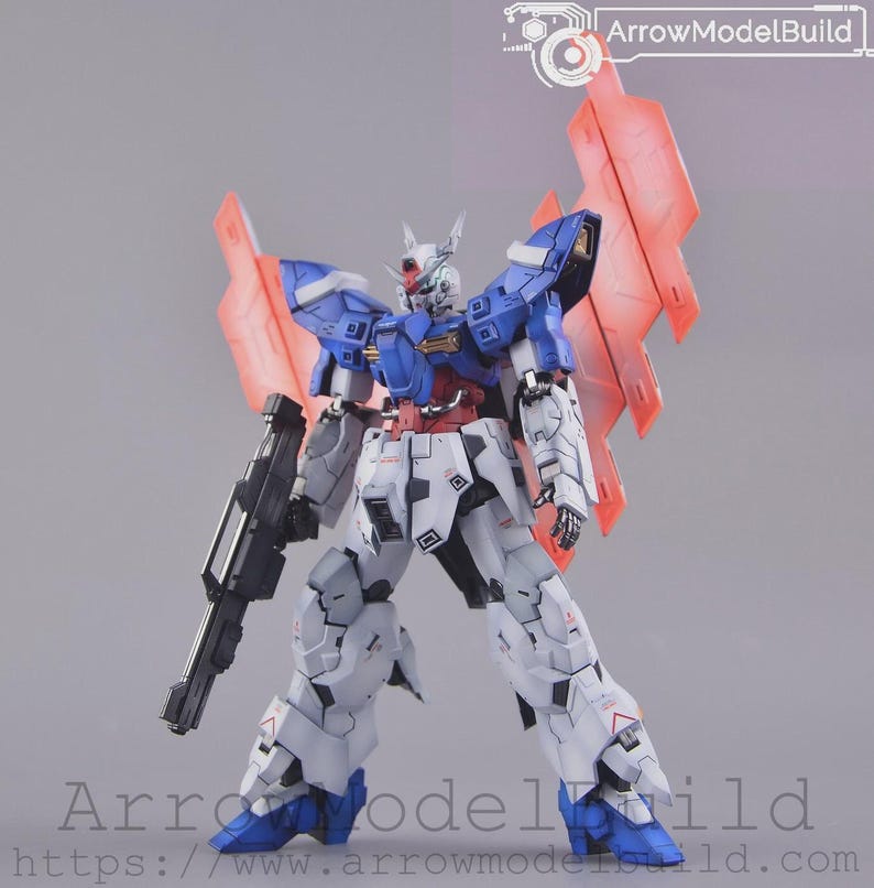May include: A detailed robot model in blue, white, red, and grey. It features large red wings and a black gun. The robot is posed with legs apart. The text "ArrowModelBuild" is visible. The model is a detailed representation.