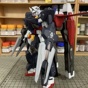 Puede incluir: Modelo detallado de un robot Gundam, con una combinaci&oacute;n de colores azul marino, blanco, rojo, amarillo y gris. El modelo tiene extremidades grandes y articuladas y est&aacute; equipado con un escudo y armas. El modelo est&aacute; sobre una superficie cuadriculada.