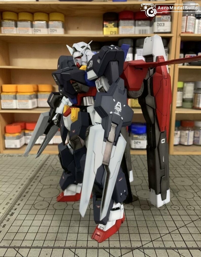 Puede incluir: Modelo detallado de un robot Gundam, con una combinaci&oacute;n de colores azul marino, blanco, rojo, amarillo y gris. El modelo tiene extremidades grandes y articuladas y est&aacute; equipado con un escudo y armas. El modelo est&aacute; sobre una superficie cuadriculada.