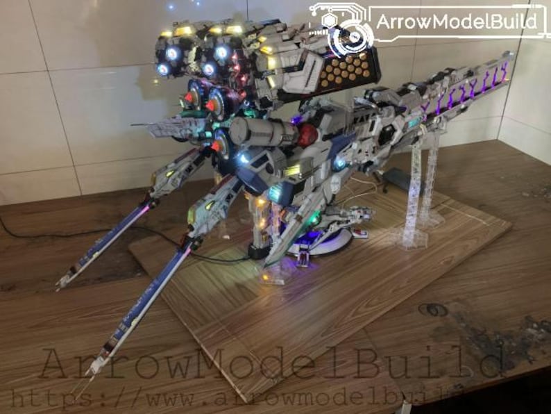 May include: A detailed model of a futuristic spacecraft, featuring a complex design with multiple sections and illuminated lights. The model is primarily white, gray, and blue, with accents of red and purple. The model is displayed on a wooden surface.