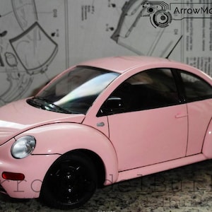 May include: A pink model car with black wheels and a black roof. The car has a classic design, with a rounded body and a small antenna. The model is set against a background of blueprints and text.