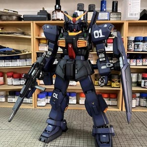 Pu&ograve; includere: Modello dettagliato di un robot mecha blu scuro e nero con accenti arancioni e gialli. Il robot &egrave; armato con un fucile e uno scudo e presenta il numero "01" sulla spalla e sulla gamba. Il modello &egrave; su una superficie a griglia.