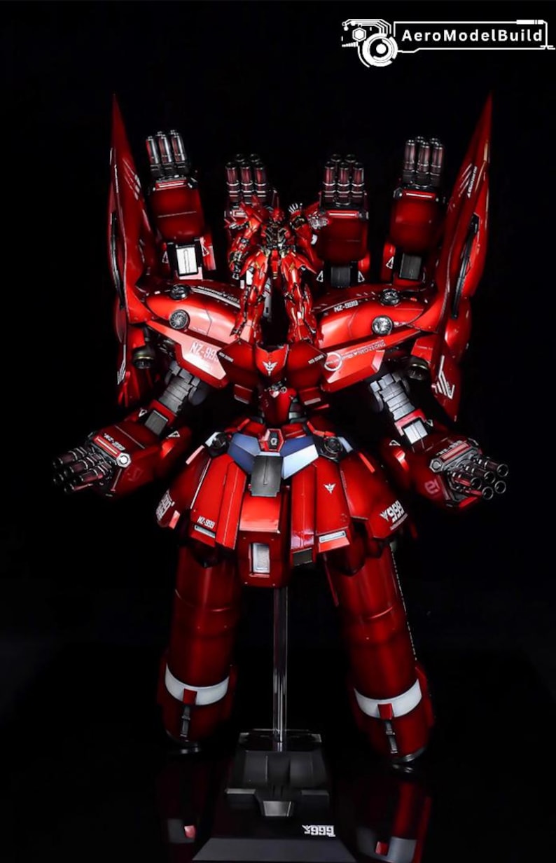 May include: A detailed, red model of a mobile suit robot with multiple weapons and armor plating. The model has a glossy finish and is displayed against a black background. The text "AeroModelBuild" is visible in the top right corner.