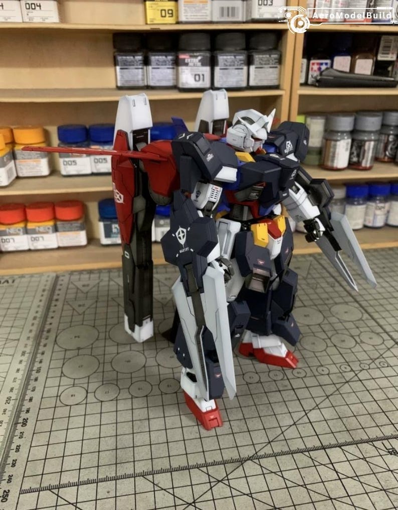 Puede incluir: Maqueta detallada de un robot Gundam, con una combinaci&oacute;n de colores azul marino, blanco, rojo y amarillo. El robot tiene extremidades grandes y articuladas, una cabeza con cresta blanca y est&aacute; equipado con un escudo y una espada. El modelo est&aacute; sobre una superficie cuadriculada.