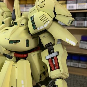 May include: A detailed, light yellow model of a robot with intricate mechanical details. The model features red cylindrical components, black accents, and the word "TITANS" printed on the lower section. The model is set against a blurred background.