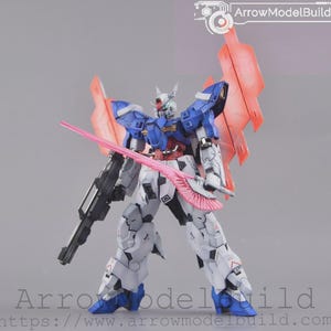 May include: A detailed model robot with blue, white, and grey armour, holding a pink sword and a black gun. The robot has red accents and large pink wings. The text "ArrowModelBuild" is visible in the top right corner.