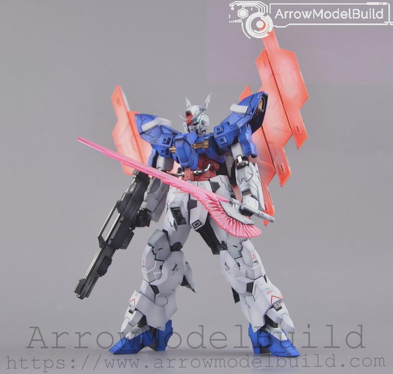 May include: A detailed model robot with blue, white, and grey armour, holding a pink sword and a black gun. The robot has red accents and large pink wings. The text "ArrowModelBuild" is visible in the top right corner.