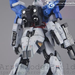 May include: A detailed model kit of a mecha robot, with a colour scheme of white, blue, black, and red. The robot has intricate mechanical details, including panels, vents, and weapon attachments. The image includes the text "ArrowModelBuild".