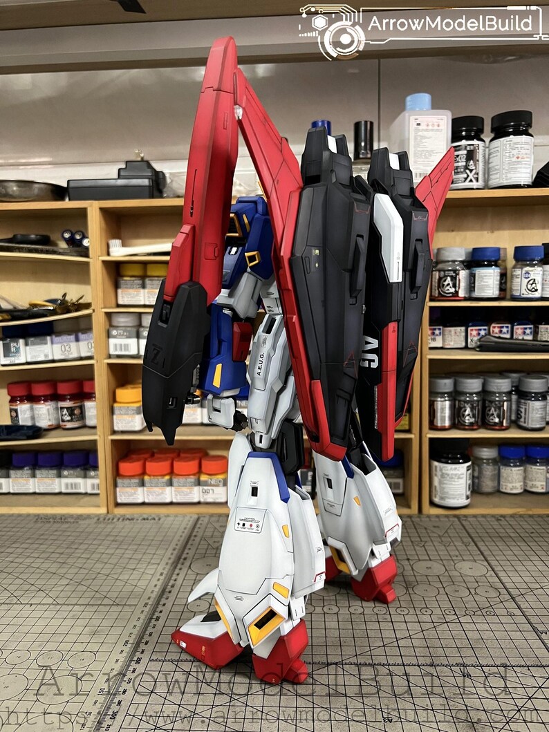 May include: A detailed model of a robot with red, black, white, and blue accents. The robot has large wings and is posed on a gray surface. The model is a complex build, showcasing intricate details and design.