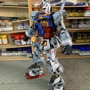 K&ouml;nnte beinhalten: Ein detailliertes Modell eines Gundam-Roboters mit einem Farbschema aus Wei&szlig;, Blau, Rot und Gelb. Das Modell steht aufrecht und zeigt komplizierte mechanische Details und Linien. Die F&uuml;&szlig;e des Roboters sind rot und wei&szlig;, und das Modell steht auf einer Rasteroberfl&auml;che.