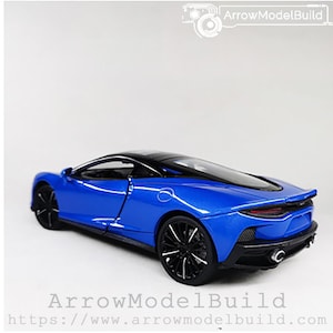 Op de afbeelding: Een blauwe model sportwagen met zwarte wielen en een zwart dak. De auto heeft een strak design en staat tegen een witte achtergrond. De tekst "ArrowModelBuild" en een websiteadres zijn zichtbaar.
